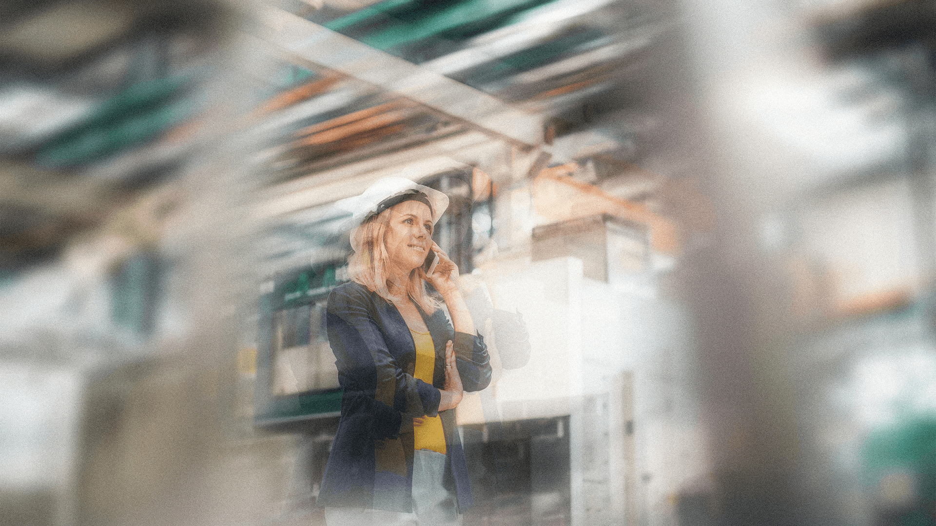 Woman in a hard hat talking on phone in an industrial building